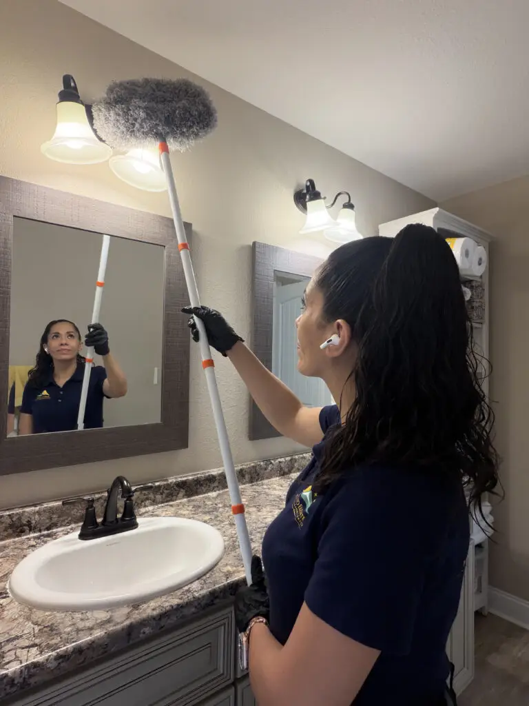 Professional house cleaner dusting bathroom light fixture in Maryville TN